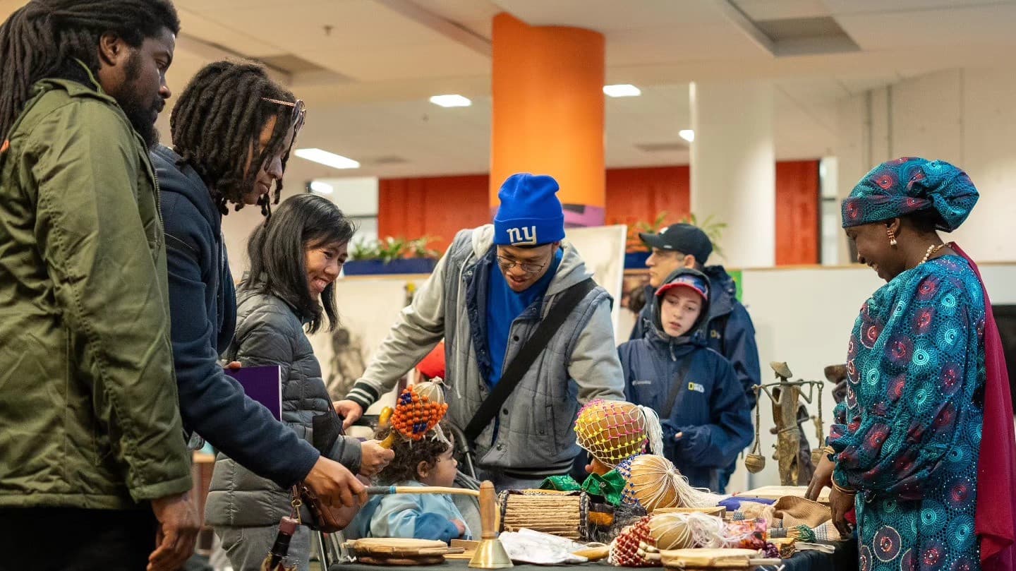 Visitors explore musical instruments and cultural objects displayed on a table with a presenter.