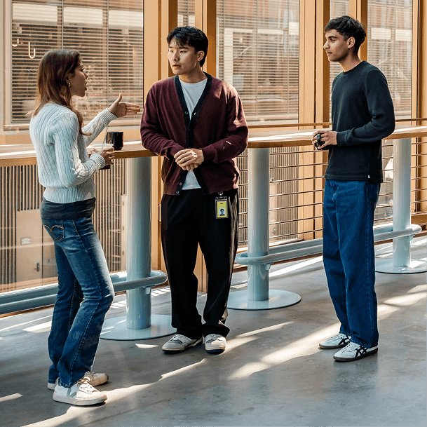 Three colleagues talking in a sunlit office.