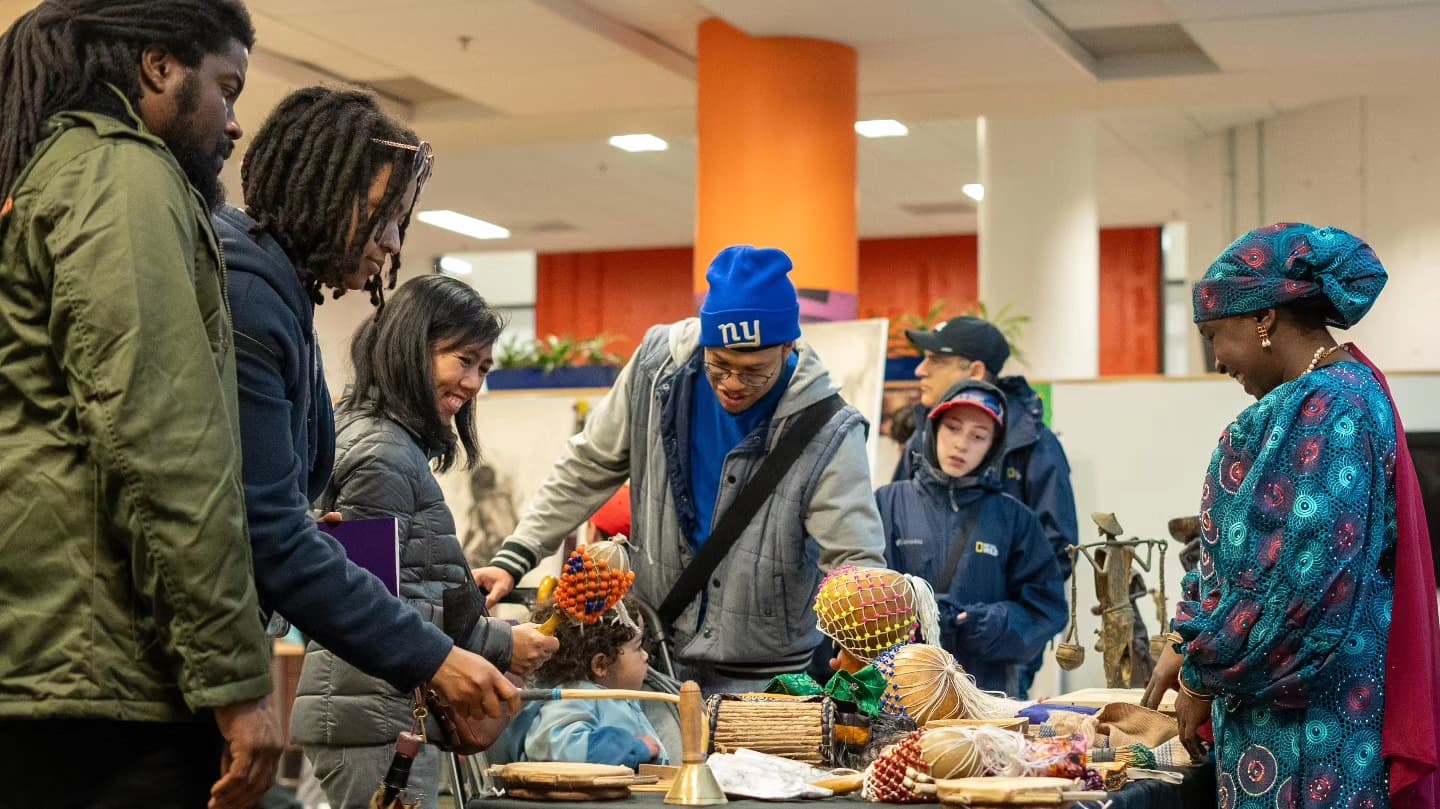 Visitors explore musical instruments and cultural objects displayed on a table with a presenter.